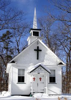 an old white church with a cross on the front door and steeple in winter