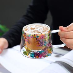 a person holding a coffee cup with flowers on the inside and outside, while sitting at a table