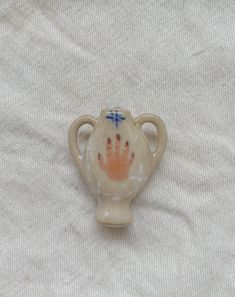 a small ceramic vase sitting on top of a white cloth covered table with a cross painted on it