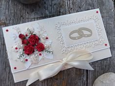 a white card with red roses and two wedding rings on it, sitting on a wooden table