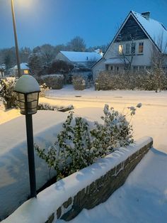 a snow covered street with a lamp post and house in the background