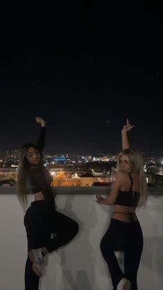 two women standing next to each other on top of a roof