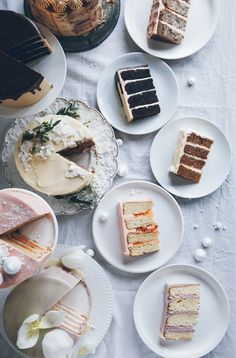 there are many different types of cakes on the table with white plates and flowers around them