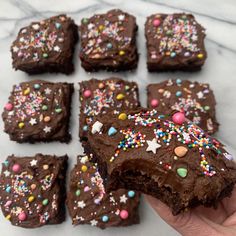 a hand holding a piece of chocolate brownie with sprinkles