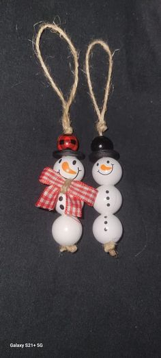 two snowmen wearing hats and scarfs are hanging from twine strings on a black surface