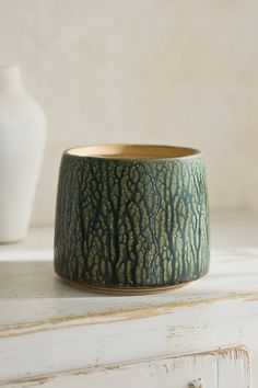 a green and white vase sitting on top of a table next to a white vase