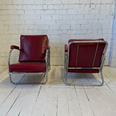 two red chairs sitting next to each other on top of a white brick wall and wooden floor