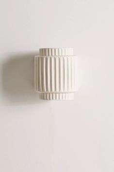 a white vase is hanging on the wall next to a light fixture that looks like pleated paper