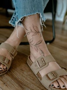 a woman's foot with tattoos on it and her feet in sandals, sitting on a wooden floor