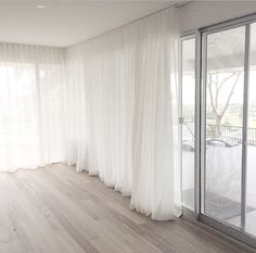 an empty room with white curtains and wood flooring on the outside, looking out onto a patio