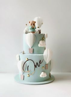 a three tiered cake decorated with hot air balloons and a teddy bear on top