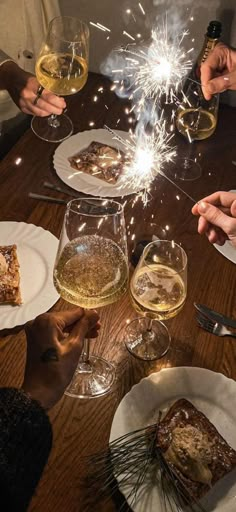 people sitting at a table with glasses of wine and sparklers in the air above them