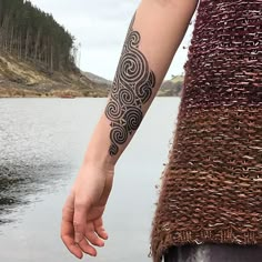 a woman with a tattoo on her arm holding the hand of another person near a body of water