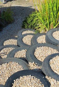 several tires are stacked on top of gravel in front of a plant and some grass