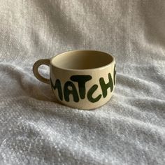 a ceramic cup with the word match painted on it sitting on a white cloth covered surface