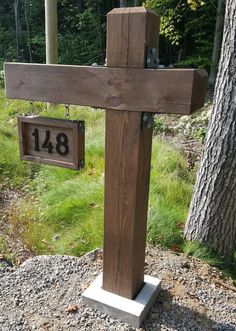 a wooden cross sitting on top of a gravel ground next to a tree and sign