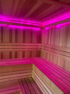 the inside of a wooden sauna with pink lights on it's walls and floor