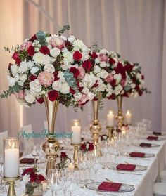 the table is set with white and red flowers in vases, candles, and wine glasses