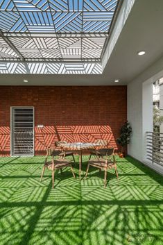 an outdoor dining area with grass on the floor and skylight above it, in front of a brick wall