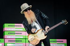 a man with a long beard playing an electric guitar on stage in front of stacks of green and pink boxes