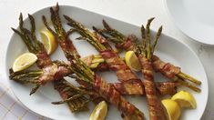 asparagus spears with bacon and lemon wedges on a white plate