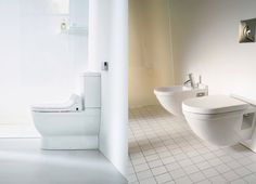 two toilets and a sink in a white bathroom with tile flooring on the walls