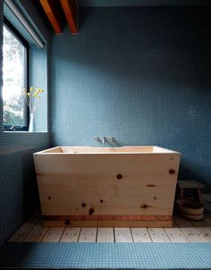 a bath tub sitting next to a window in a blue tiled bathroom with wood flooring