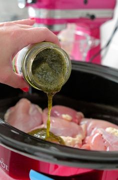 someone pouring sauce into an open crock pot filled with raw chicken and broccoli