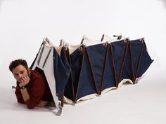 a man sitting on the ground next to a blue and white tent with two doors open