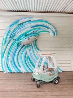 a small car is parked in front of a wall with surfboards painted on it