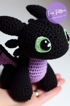 a small crocheted black dragon sitting on top of a person's hand