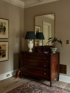 a dresser with two lamps on top of it next to a mirror and framed pictures