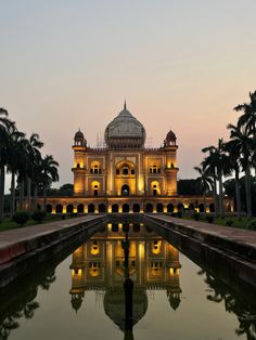 an ornate building lit up at night with its reflection in the water and palm trees