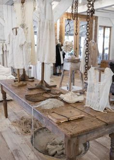 an old wooden table with clothes on it in a room filled with white dresses and other items