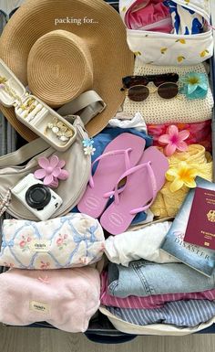 an open suitcase filled with clothes and hats, passport, sunglasses, and other items