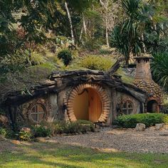 a small house made out of logs in the middle of some trees and grass with plants growing on top