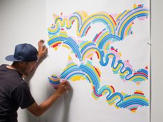 a man is drawing on a wall with colorful lines and shapes in the background,