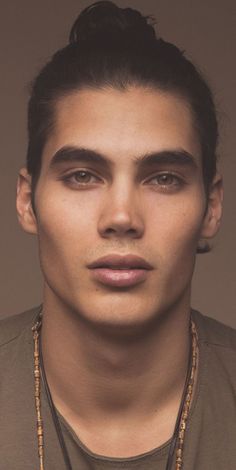 a young man wearing a necklace and looking at the camera with an intense look on his face