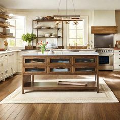 a large kitchen with wooden floors and white cabinets, an island in the middle is surrounded by open shelving