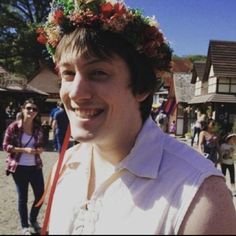 a man with a flower crown on his head smiles at the camera while people walk by