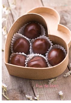 four chocolates in a heart shaped box on a wooden table next to dried flowers