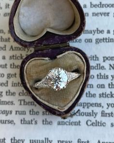 an engagement ring in a heart shaped box on top of a piece of paper with writing underneath it