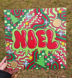 someone holding up a piece of art with the word noel painted in red and green