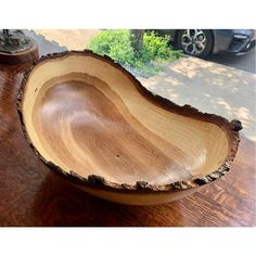 a wooden bowl sitting on top of a wooden table next to a black car in the background