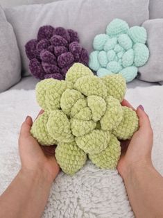 a person holding some crocheted flowers in their hands on a white blanket with pillows behind them