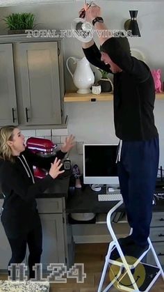 a man standing on a stool next to a woman in front of a computer desk