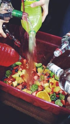 two people are pouring water into a red container filled with fruit and veggies