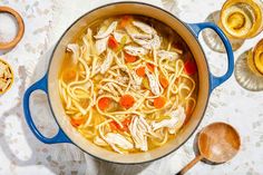 a pot filled with chicken noodle soup on top of a table next to wooden spoons