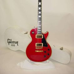 a red electric guitar sitting on top of a white table next to a wooden case