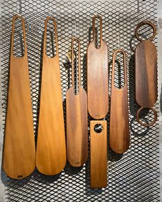 five wooden cutting boards hanging from hooks on a wire mesh wall with strings attached to them